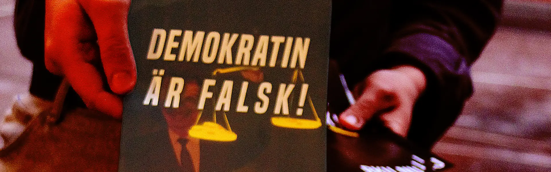 En person r&auml;cker &ouml;ver ett flygblad med texten "Demokratin &auml;r falsk!" p&aring;