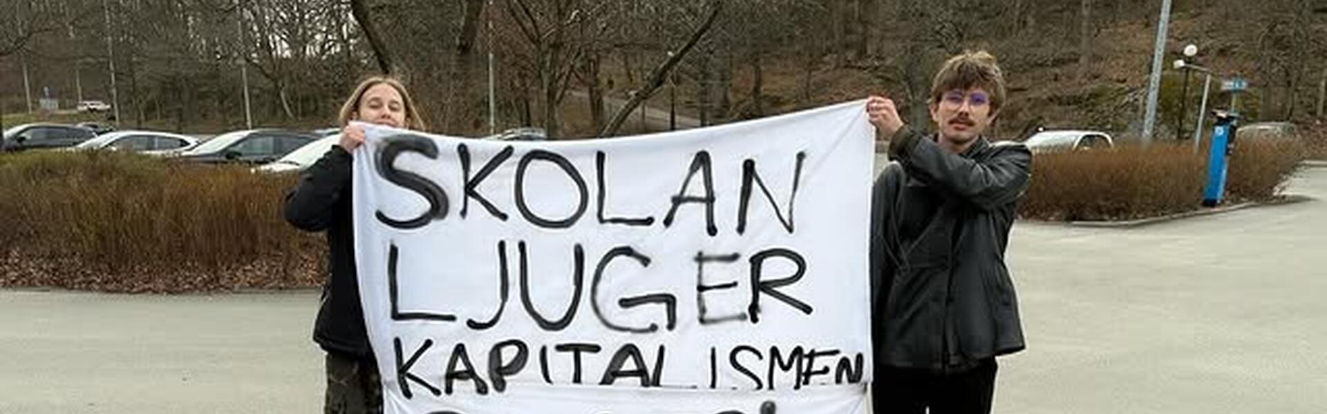 Bild på två personer som håller upp en banderoll där det är sprejmålat "Skolan ljuger, Kapitalismen suger"