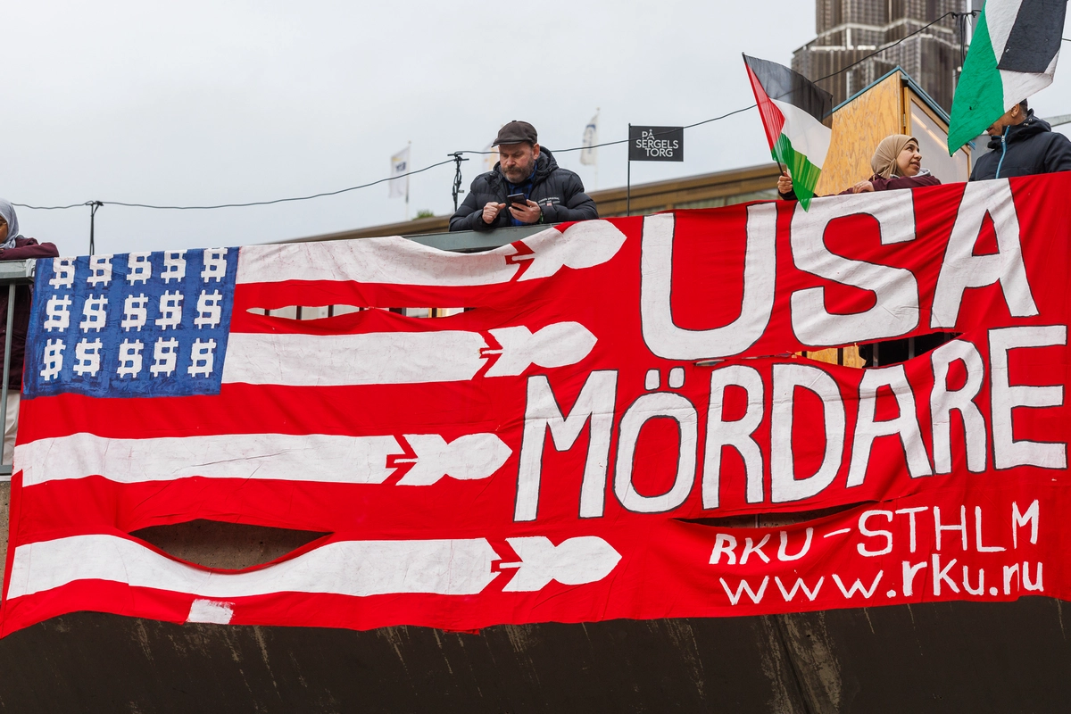 Bild p&aring; en banderoll d&auml;r det st&aring;r "USA m&ouml;rdare" och en stiliserad variant av USA:s flagga med dollartecken ist&auml;llet f&ouml;r stj&auml;rnor och komber ist&auml;llet f&ouml;r r&auml;nder.